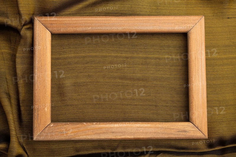 Wooden frame on smooth olive and golden silk tissue. Top view, flat lay, natural textile background and texture