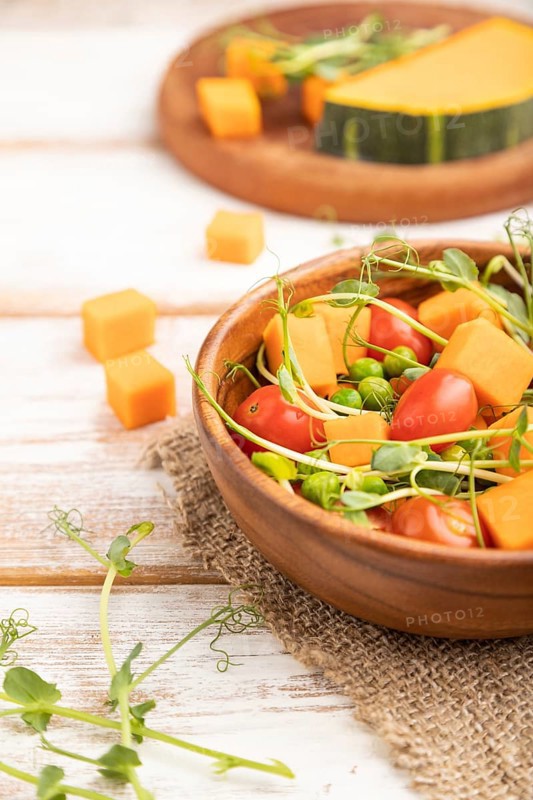 Vegetarian vegetable salad of tomatoes, pumpkin, microgreen pea sprouts on white wooden background and linen textile. Side view, close up, selective focus