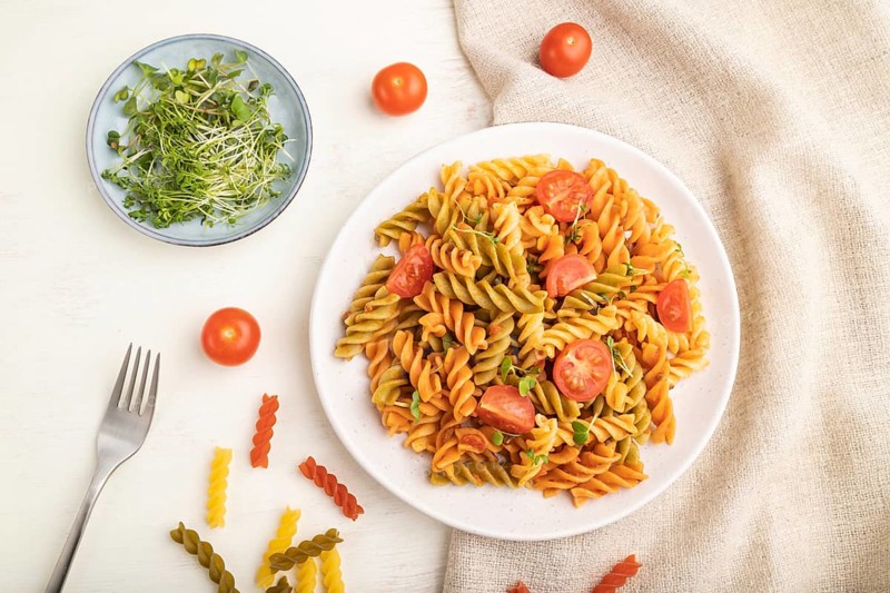 Tortiglioni semolina pasta with tomato and microgreen sprouts on a white wooden background and linen textile. Top view, flat lay, close up