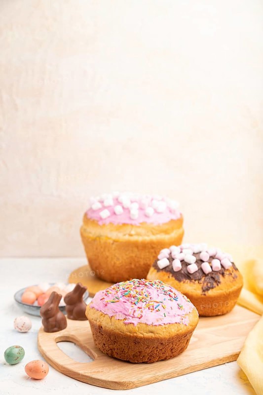 Homemade glazed and decorated easter pies with chocolate eggs and rabbits on a white concrete background and yellow textile. Side view, copy space, selective focus