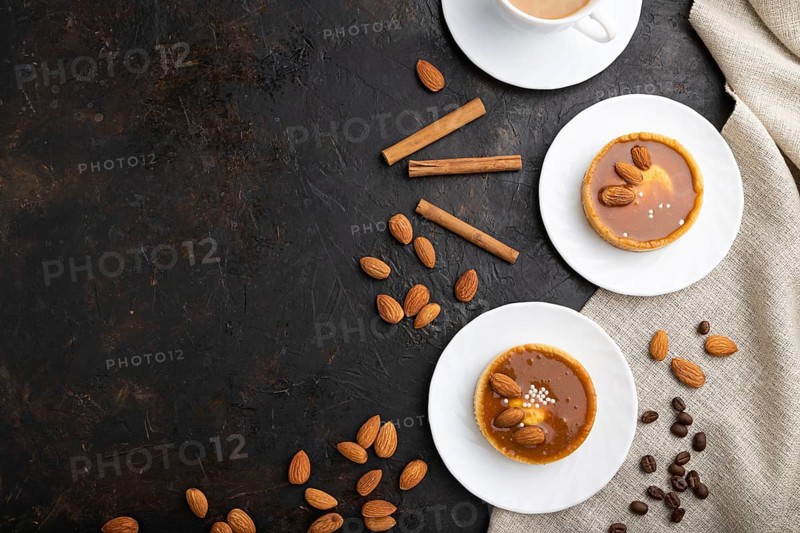 Sweet tartlets with almonds and caramel cream with cup of coffee on a black concrete background and linen textile. top view, flat lay, copy space