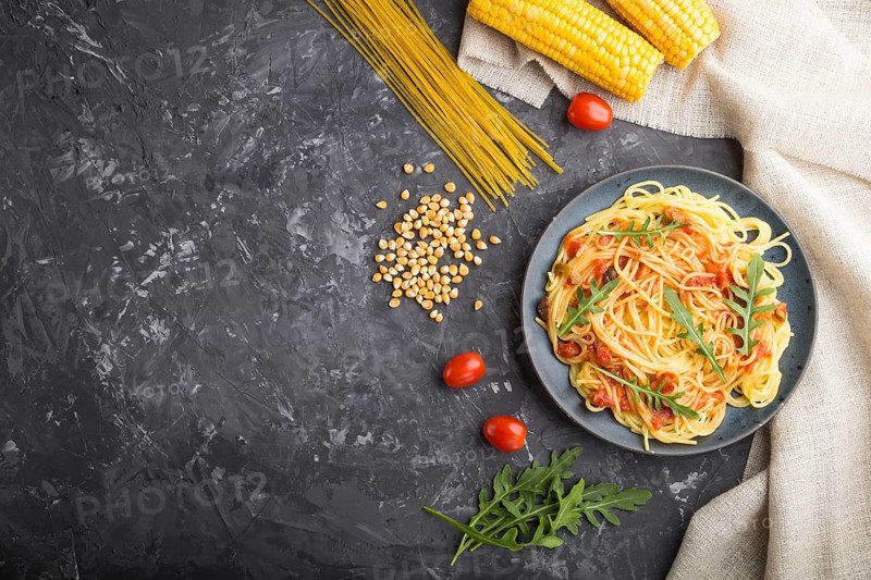 Corn noodles with tomato sauce and arugula on a black concrete background and linen textile. Top view, flat lay, copy space