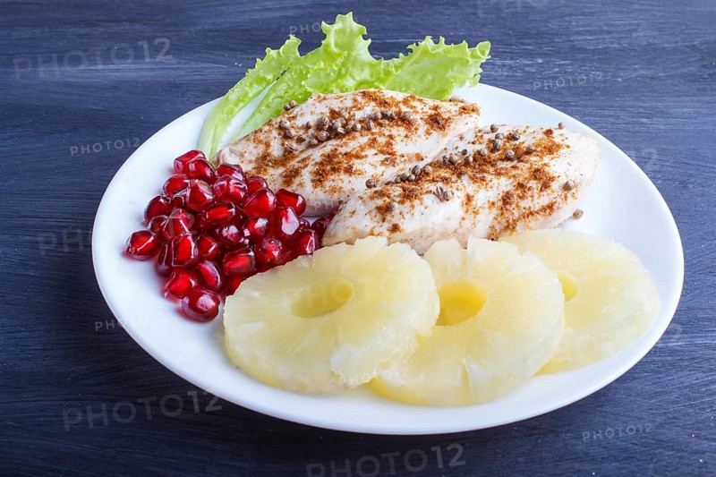 Fried chicken fillets with lettuce, pineapple and pomegranate seeds on black wooden background, copy space, close up