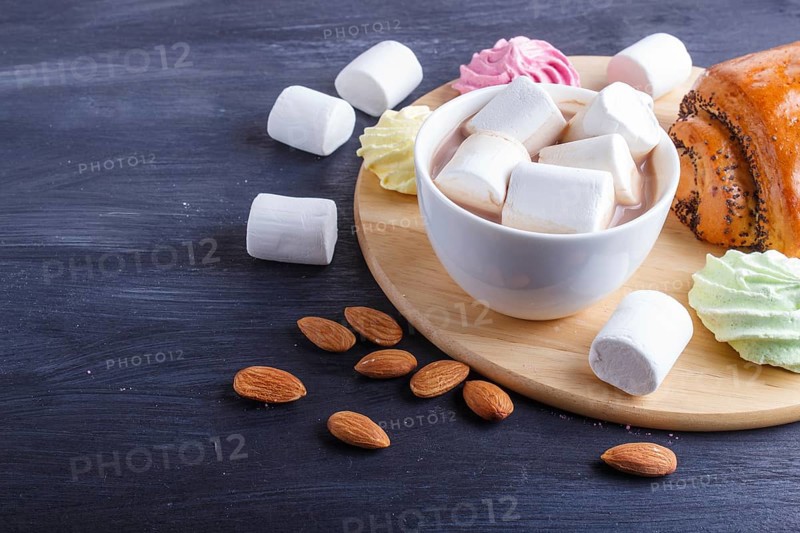 A cup of hot chocolate with marshmallow, bun and meringues on black wooden background. close up, copy space