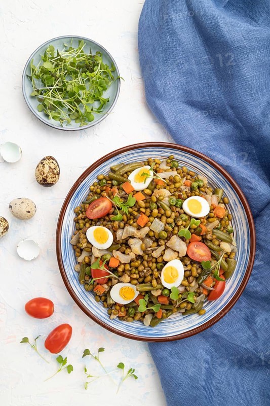 Mung bean porridge with quail eggs, tomatoes and microgreen sprouts on a white concrete background and blue textile. Top view, flat lay, close up
