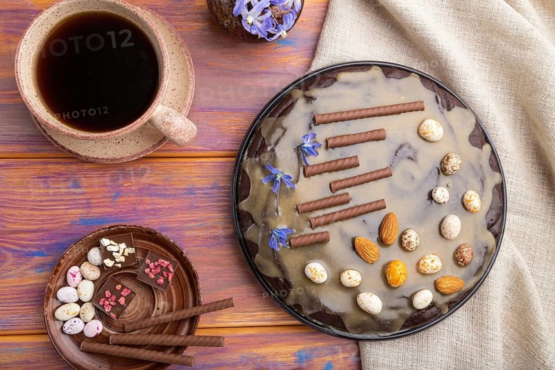 Homemade chocolate brownie cake with caramel cream and almonds with cup of coffee on a colored wooden background and linen textile. top view. flat lay, close up