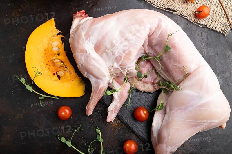 Whole raw rabbit with pumpkin, tomatoes, pea sprouts on a black concrete background and linen textile. Top view, flat lay, close up
