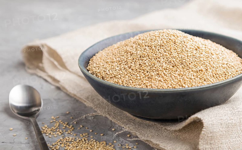 Blue ceramic bowl with raw white quinoa seeds on a gray concrete background and linen textile. Side view, close up, selective focus