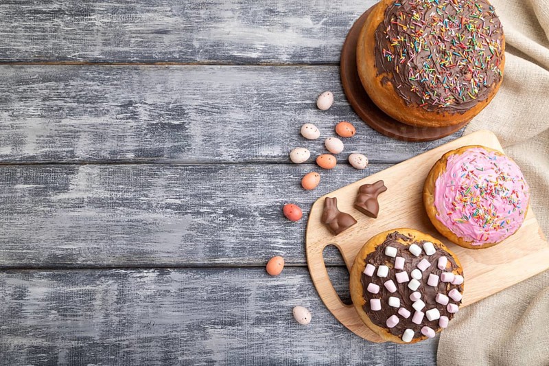 Homemade glazed and decorated easter pies with chocolate eggs and rabbits on a gray wooden background and linen textile. top view, flat lay, copy space