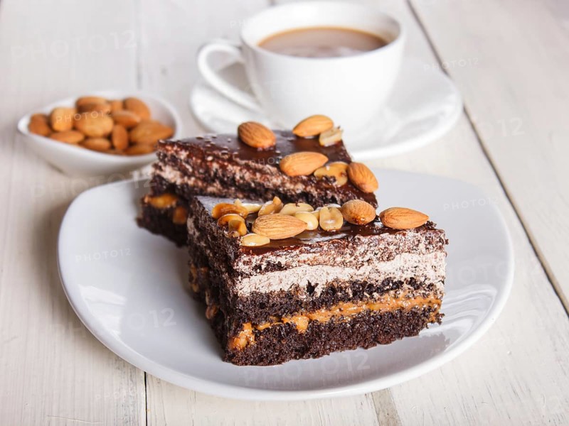Chocolate cake with caramel, peanuts and almonds on a white wooden background. cup of coffee, top view, close up