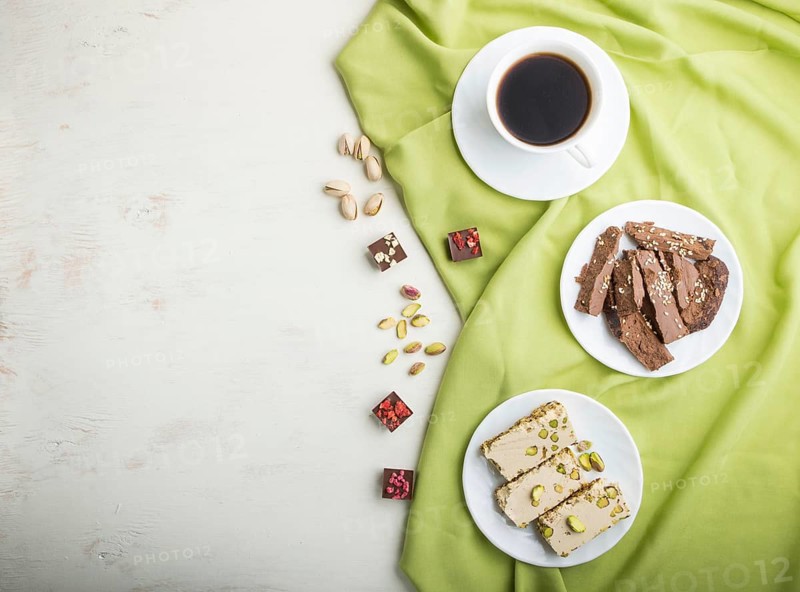 Traditional arabic sweets sesame halva with chocolate and pistachio and a cup of coffee on a white wooden background and green textile. top view, flat lay, copy space