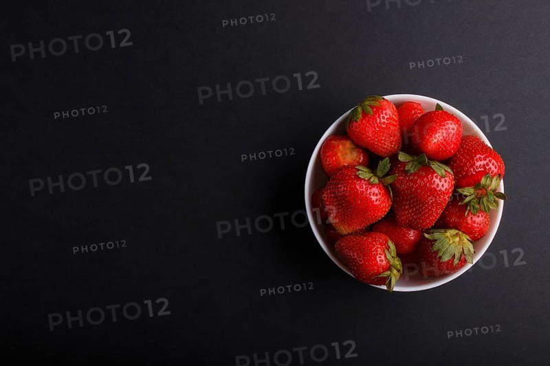 Fresh red strawberry in white bowl on black background. top view, flat lay, copy space
