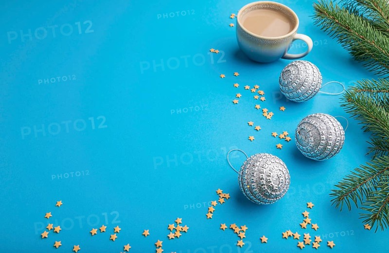 Christmas or New Year composition. Decorations, silver balls, fir and spruce branches, cup of coffee, on a blue paper background. Side view, copy space