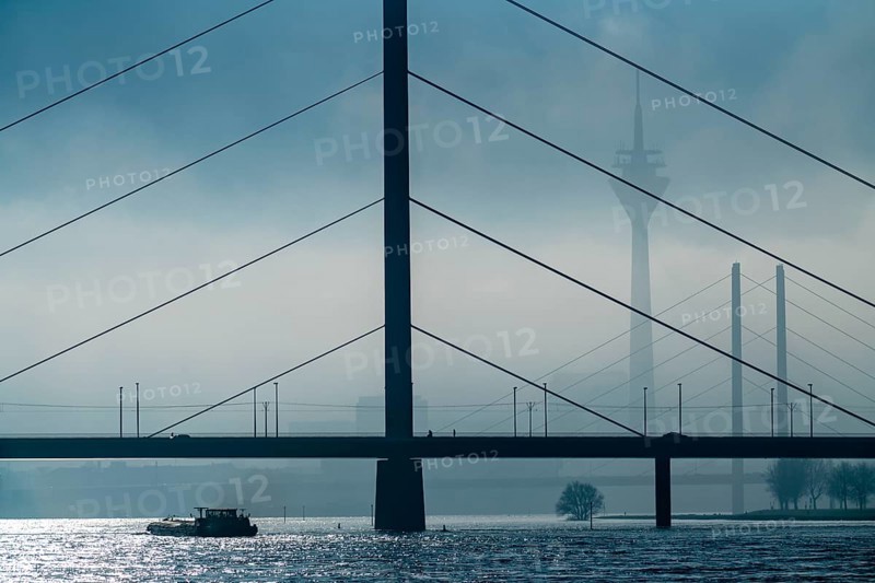 Dense fog slowly lifting, cargo ships on the Rhine near Düsseldorf, in front the Oberkassler Bridge, behind it the Rheinknie Bridge, Rhine Tower, North Rhine-Westphalia, Germany, Europe