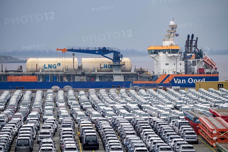 Parking space for import vehicles, hundreds of Hyundai Ioniq, electric cars, waiting for onward transport, behind them, on the Weser, the dredger, the hopper dredger, suction dredger, Vox Ariane, which holds the tug to a certain depth, at the EUROGATE container terminal in the overseas port of Bremerhaven, Lower Saxony, Germany, Europe