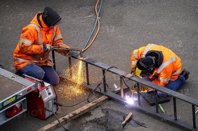 Locksmith at work, cutting and welding, on a workpiece in an industrial plant, a metal ladder is split with a welding torch, a welder fixes a ladder rung with a welding machine