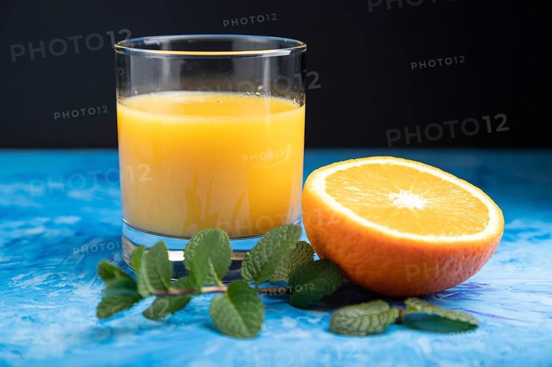 Glass of orange juice with mint on a black and blue background. Hard light, contrast. Side view, close up