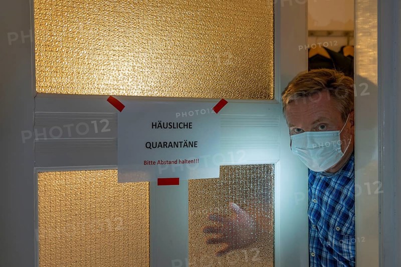 Symbolic image Domestic quarantine, man is in isolation at home due to a suspected corona infection, warning sign for visitors on the front door, communicating with a visitor through the door