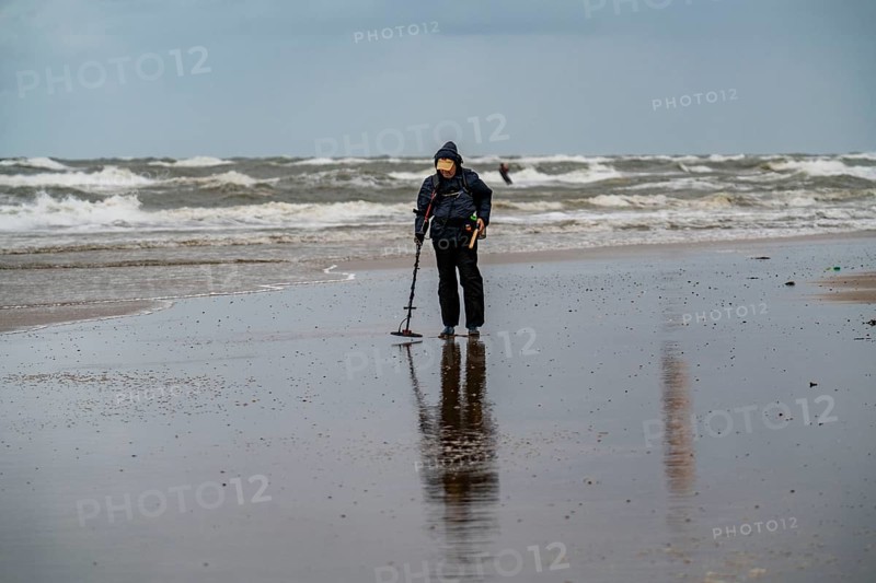 Treasure hunter, man with metal detector on the beach, dark storm clouds, autumn at the North Sea in North Holland, near Egmond aan Zee, Netherlands