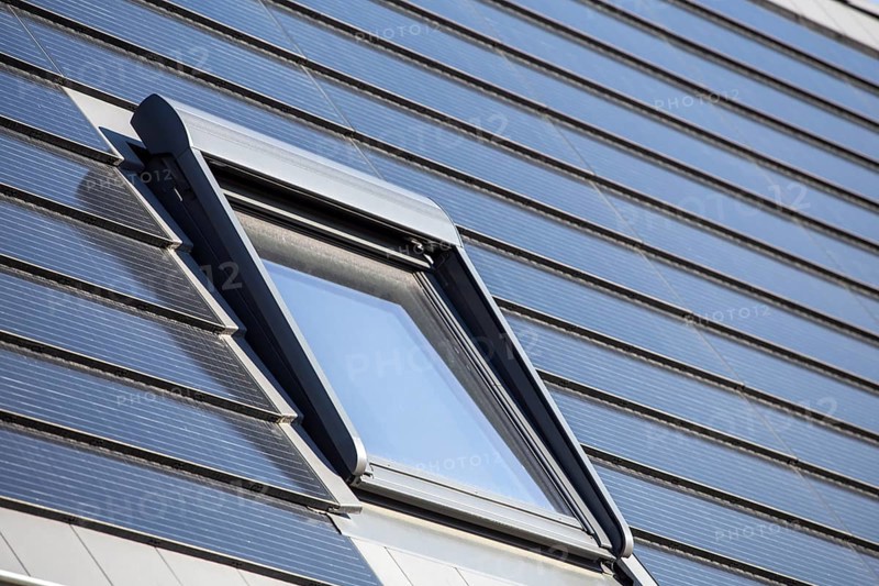 Roof window on a detached house with solar roof tiles. Solar tiles are a beautiful and high-quality alternative to conventional photovoltaic systems