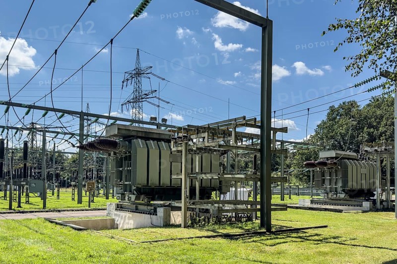 In front and on the right large transformer transformer transformer transformer in transformer station, top left hanging suspended power lines in the background overhead line mast high-voltage mast power mast supporting mast suspension of overhead electrical line overhead line for transmission of electrical energy energy supply, Germany, Europe