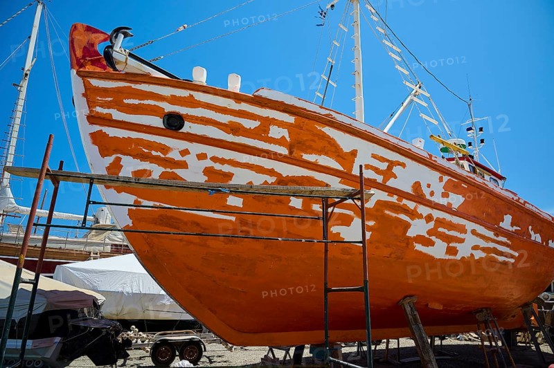 A wooden boat is being restored in dry dock, with the orange and white colour being renewed, Patmos Marine, boatyard, Diakofti, Patmos, Dodecanese, Greek Islands, Greece, Europe