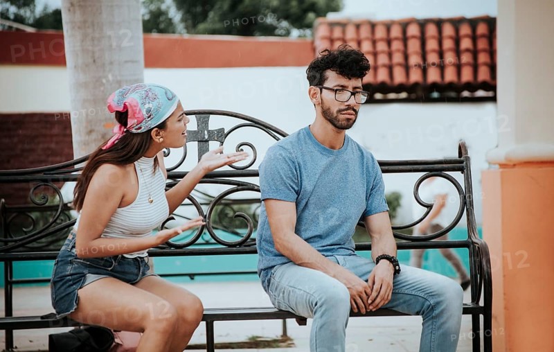 Couple sitting on a park bench arguing. A young couple arguing sitting in a park, Concept of aggressive couples in the park. Upset couple arguing on park bench