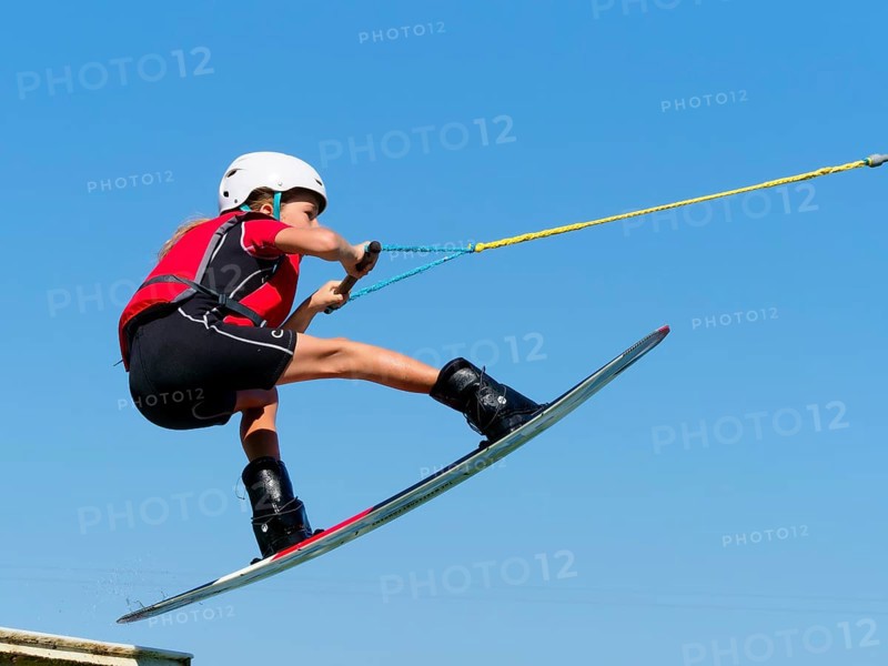 Boy or girl, jump over jump with wakeboard, red life jacket and water sports, water skiing in the wake park