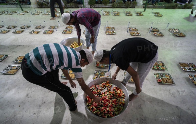 Volunteers distribute and arrange rows of 'iftar' meal for devotees to break their fast, during the holy month of Ramadan, at Burha Jame Masjid, on March 13, 2024 in Guwahati, Assam, India, Asia