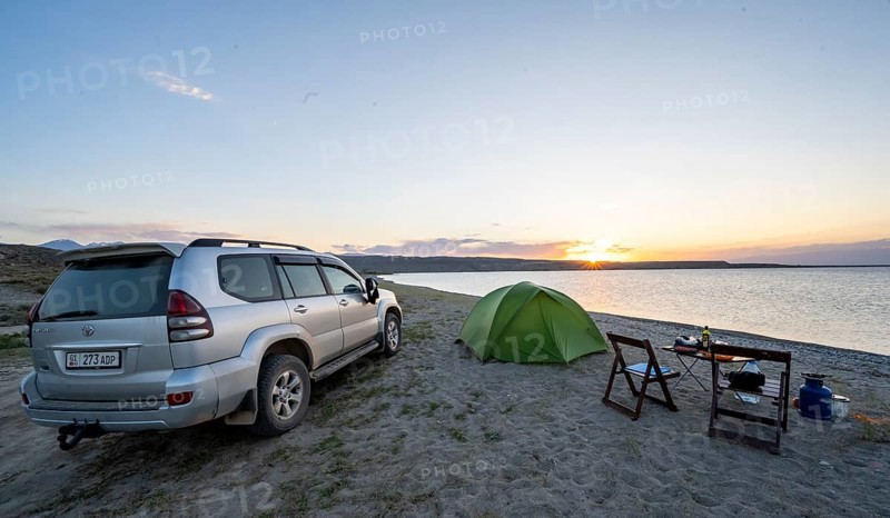 Camping on the lakeshore, off-road vehicle next to tent and camping chairs, sunset at Issyk Kul Lake, Issyk Kul, Kyrgyzstan, Asia
