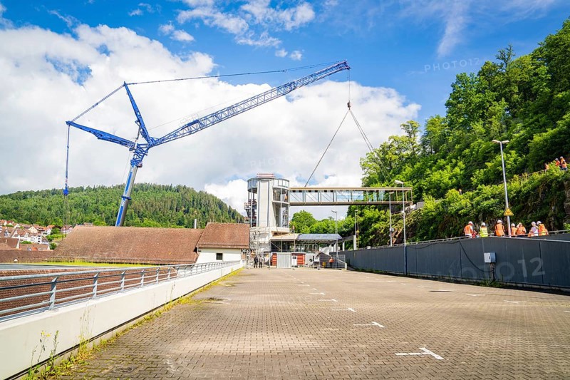 A crane lifts a bridge over a building in sunny weather with blue sky and white clouds, people watching, bridge lifting Hermann Hesse railway, Calw, Germany, Europe