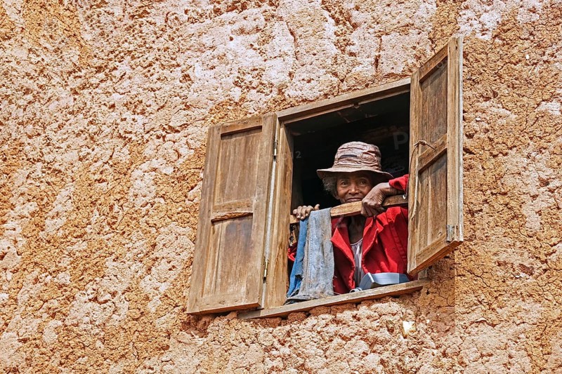 Elderly Malagasy woman looking from window in two stories mud house in the Ambositra District, Amoron'i Mania Region, Central Madagascar