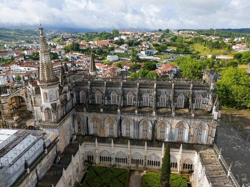 Aerial view of a Gothic cathedral with a magnificent tower and windows, an inner courtyard is visible and the surrounding area consists of a green landscape and town, aerial view, monastery, Mosteiro de Santa Maria da Vitória, 'unfinished chapels', UNESCO World Heritage Site, Batalha, Leiria, Estremadura, Portugal, Europe