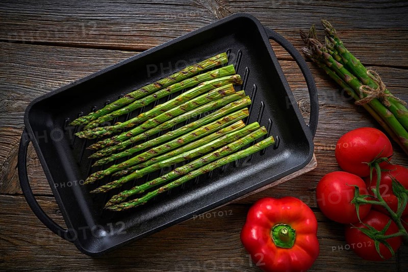 Asparagus grilled on cast iron grill pan on wood table with tomatoes and pepper