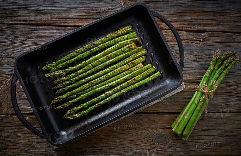 Asparagus grilled on cast iron grill pan on wood table with tomatoes and pepper