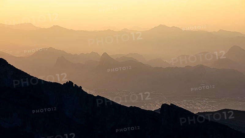 View from the mountain plateau Al Hayl into the valley, below the village of Ghul, behind in the haze the mountains of the Hajar range, Arabian Peninsula, Sultanate of Oman