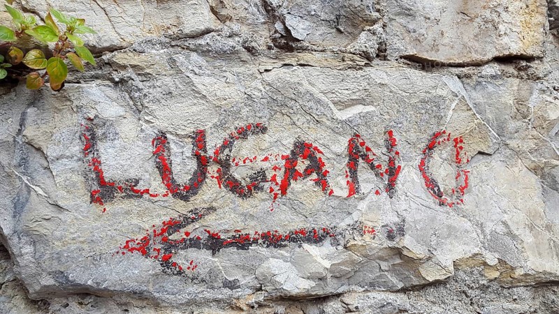 Hand painted red sign on a rock indicating the direction to Lugano, Switzerland, on Sentiero delle Olive that leads from the village of Gandria to Lugano, Europe