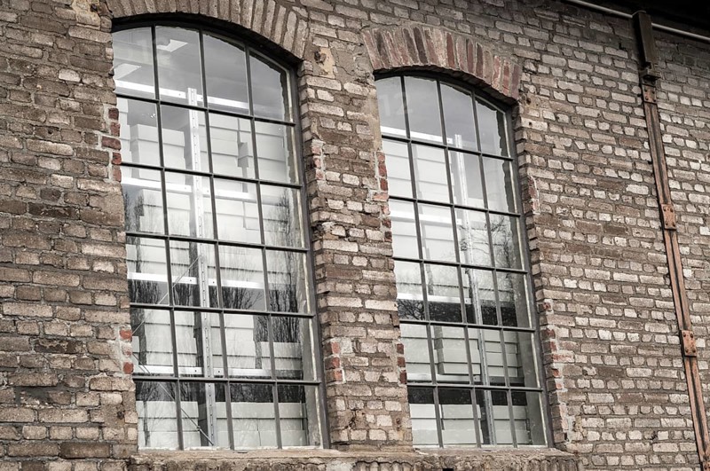 Close-up of two arched industrial windows with metal grids reflecting an empty white room in an old brick wall
