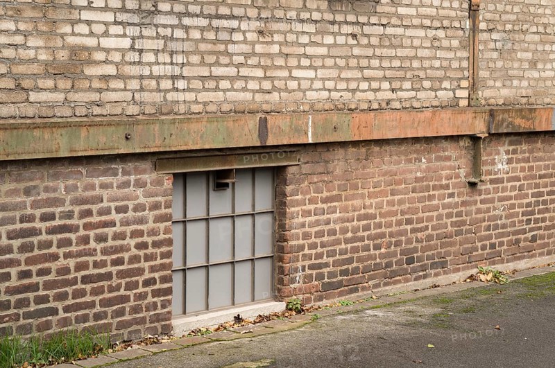 Frosted glass basement window illuminating a weathered industrial brick wall building, showcasing urban decay and architectural texture