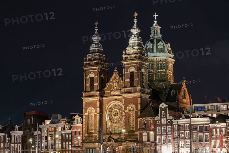 Illuminated church with striking towers and neighbouring buildings at night, Amsterdam, Netherlands