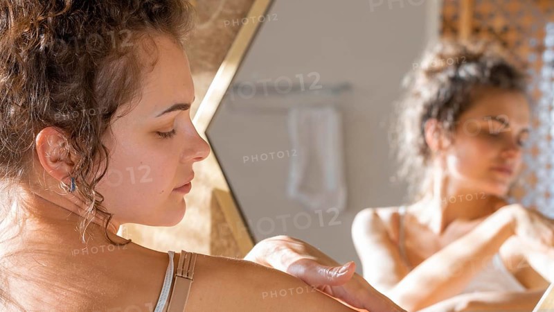 Woman looking mirror applying cream hands