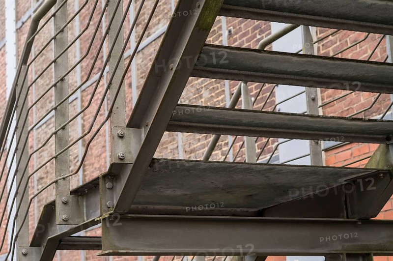 Metal fire escape with caged mesh wire alongside red brick building provides emergency exit route