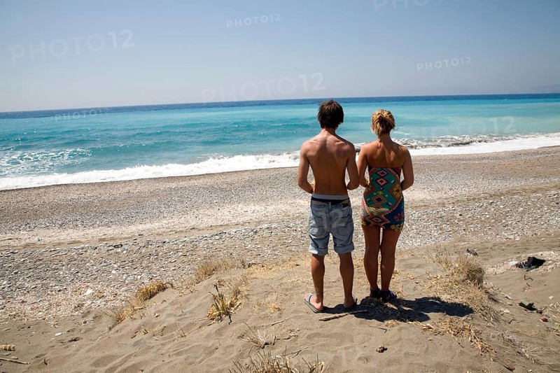 Model released brother and sister twins stand on sandy beach looking out to sea, Rhodes, Greece, Europe