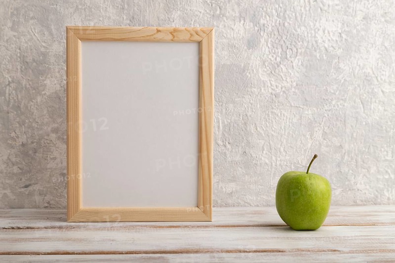 White wooden frame mockup with green apple on gray concrete background. Blank, vertical orientation, still life, copy space