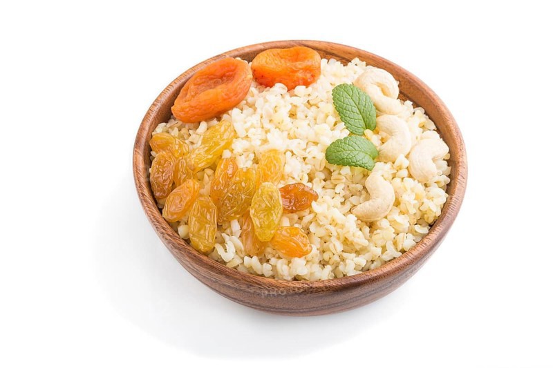 Bulgur porridge with dried apricots, raisins and cashew in wooden bowl isolated on white background. Side view, close up. Turkish traditional cuisine