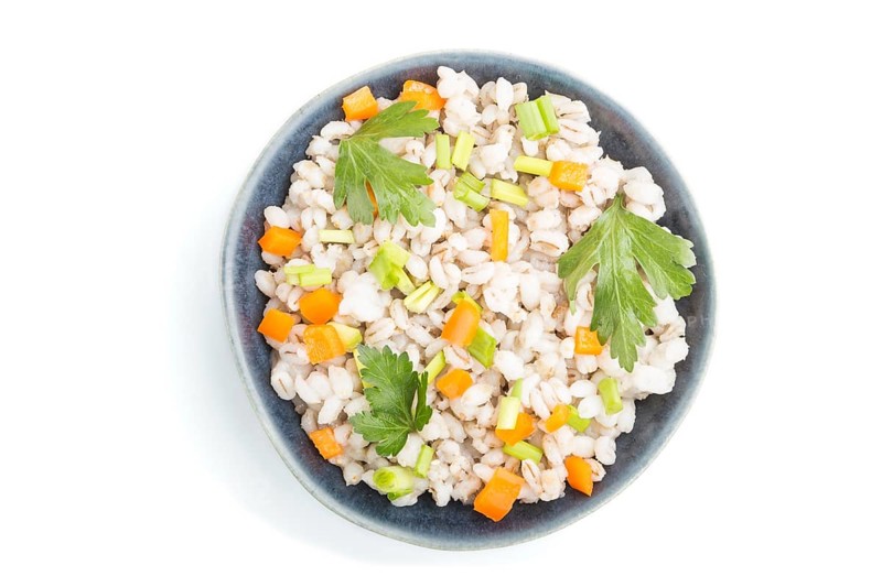 Pearl barley porridge with vegetables in blue ceramic bowl isolated on white background. Top view, flat lay, close up. Russian traditional cuisine