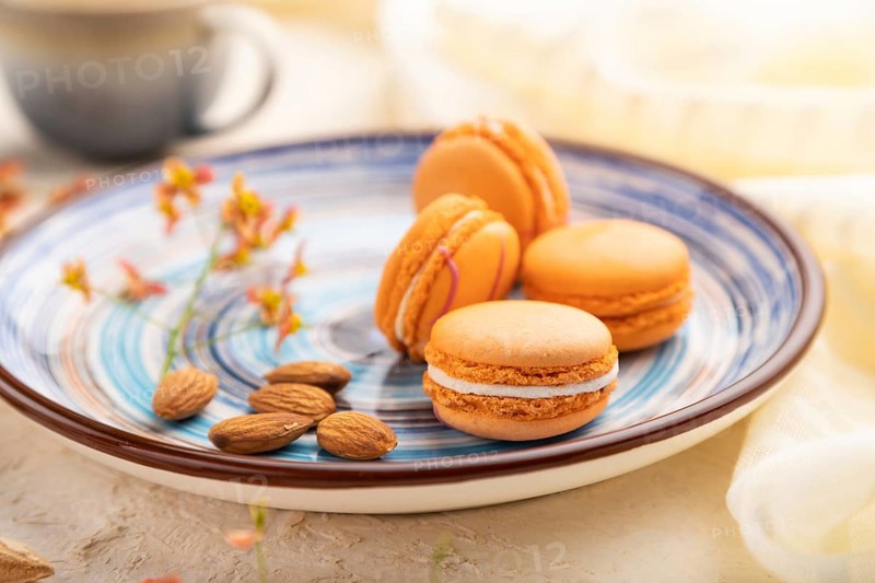 Orange macarons or macaroons cakes with cup of coffee on a white concrete background and linen textile. Side view, close up, selective focus