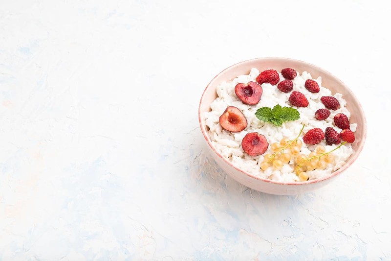 Rice flakes porridge with milk and strawberry in ceramic bowl on white concrete background. Side view, copy space, close up