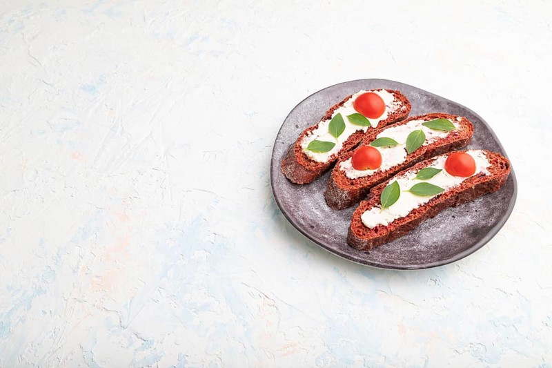 Red beet bread sandwiches with cream cheese and tomatoes on white concrete background. Side view, copy space, close up