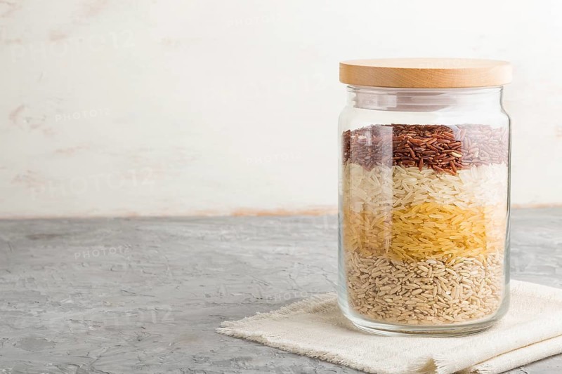 Glass jar with different kinds of rice poured in layers on a gray and white background. side view, close up, copy space. Healthy food concept